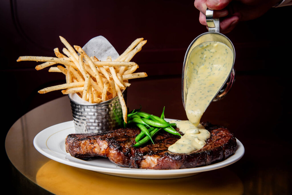 Béarnaise sauce being poured over a ribeye steak at La Plume in Toronto